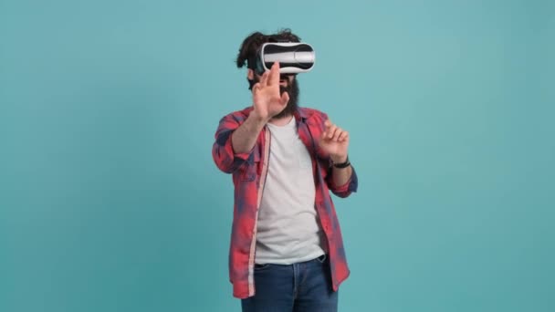 Uomo barbuto che indossa occhiali di realtà virtuale. Studio girato, sfondo turchese. - Filmati, video
