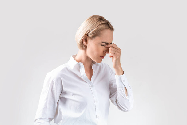 Tired female corporate employee suffering from headache on light grey studio background - Zdjęcie, obraz
