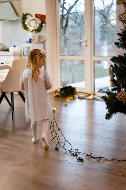 Mom and children decorate the Christmas tree with garlands and toys. The family decorates the Christmas tree. Preparing for Christmas and New Years. Children rejoice at the tree. - Foto, imagen