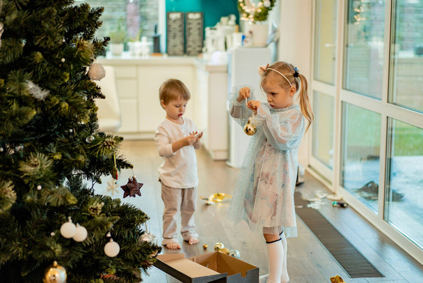 A little girl decorates a Christmas tree with garlands and toys. Children are preparing for Christmas and New Years. Merry Christmas and Happy New Year concept. - Foto, imagen