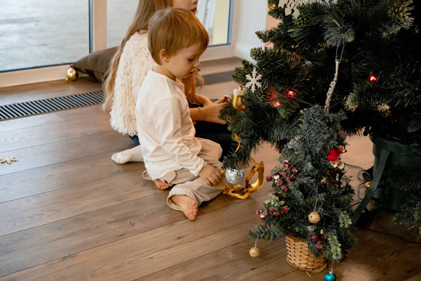 Mom and children decorate the Christmas tree with garlands and toys. The family decorates the Christmas tree. Preparing for Christmas and New Years. Children rejoice at the tree. - Photo, image
