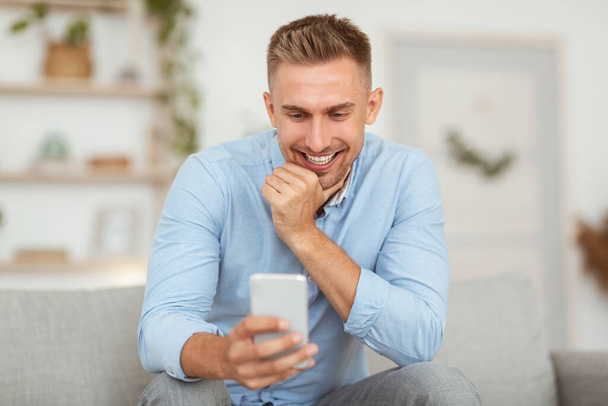 Closeup of smiling guy using mobile phone at home - Foto, imagen