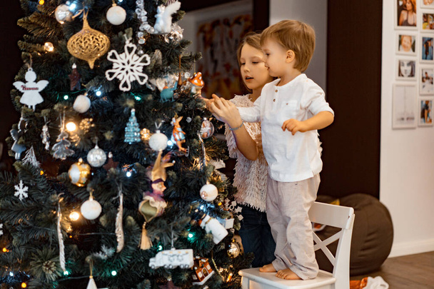 Children decorate the Christmas tree, brother and sister decorate the house for the holidays. Christmas holidays. Merry Christmas and Happy New Year concept. - Photo, image
