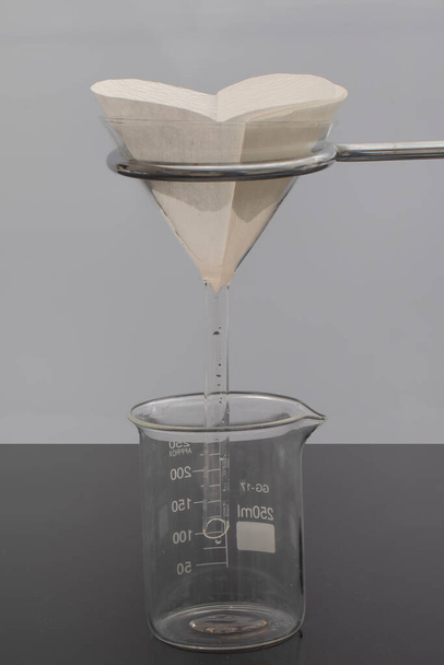 Фильтр бумаги в лаборатории. Ученые проводят химическую фильтрацию путем фильтрации через фильтрующую бумагу в стеклянной воронке, крупным планом - Фото, изображение