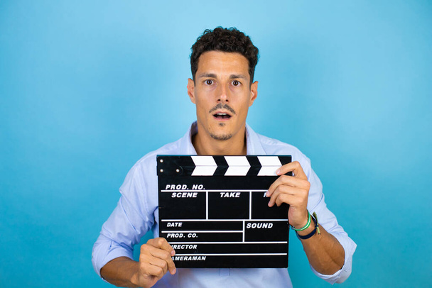 Young handsome man wearing blue shirt over isolated blue background holding clapperboard very happy - Photo, Image