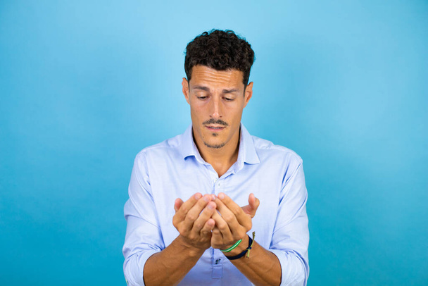 Young handsome man wearing blue shirt over isolated blue background Smiling with hands palms together receiving or giving gesture. Hold and protection - Photo, Image