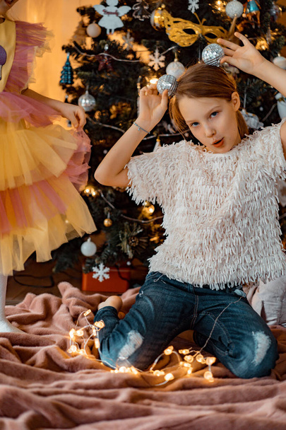 A little girl decorates a Christmas tree with garlands and toys. Children are preparing for Christmas and New Years. Merry Christmas and Happy New Year concept. - Foto, imagen