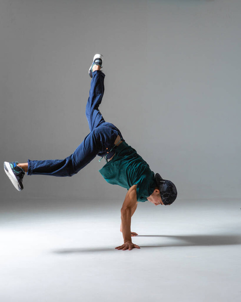 Cool guy breakdancer dances on the floor standing on hands isolated on gray background. Breakdance lessons - Valokuva, kuva