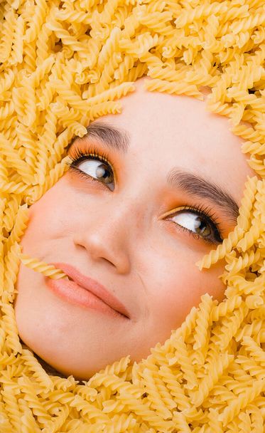 A cute girl with bright orange makeup lies in a scattering of pasta. Coronavirus pandemic preparation concept - Fotoğraf, Görsel