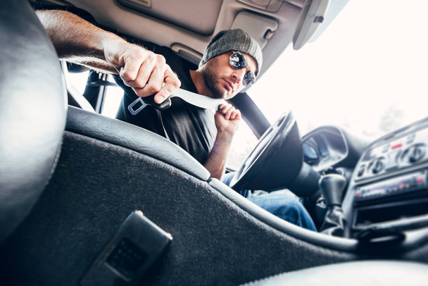 Inside view of a powerful car - a man with stubble in a hat and sunglasses fastening his seat belt before driving - Fotoğraf, Görsel