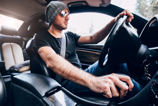 Inside view of a powerful car - a man with stubble in a hat and sunglasses drives confidently behind the wheel - manual mechanical gearbox - Fotó, kép