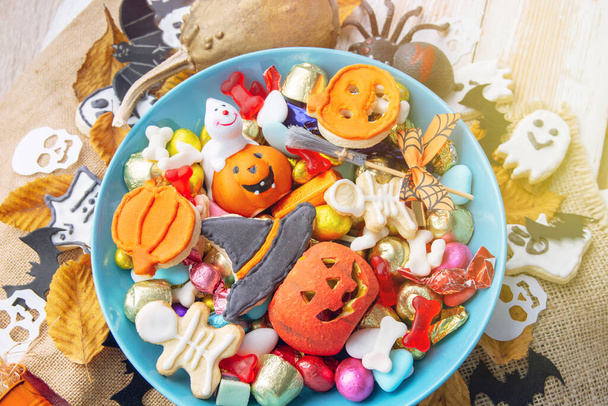 happy halloween card background, Jack o Lantern candy bowl with sweets and halloween cookies Trick or Treat surrounded by festive decor spiders, bats, skull - Fotó, kép