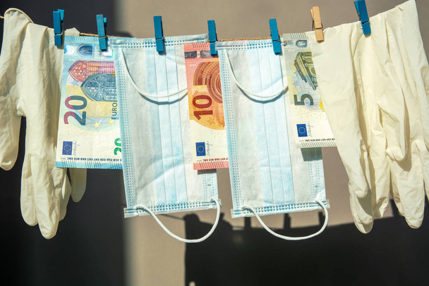 latex gloves and a medical face mask hang, euro banknotes money on clothespins hard light gray background . spending safety concept during covid coronavirus pandemic. - Zdjęcie, obraz