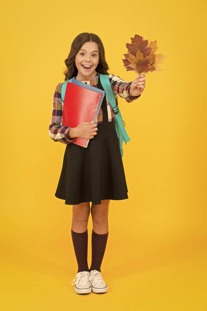 Nature lesson. Happy little child hold autumn leaves for biology lesson. Small girl smiling with lesson books and yellow foliage. Lesson can be entertaining. Back to school - Zdjęcie, obraz