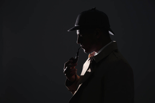 Old fashioned detective with smoking pipe on dark background. Space for text - 写真・画像