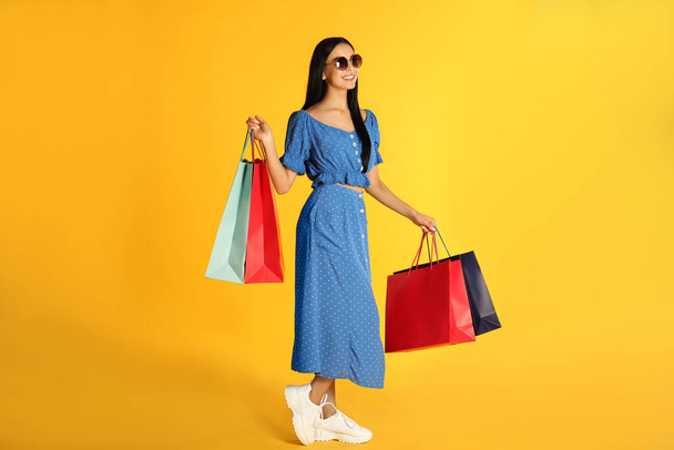 Beautiful young woman with paper shopping bags on yellow background - Foto, Imagen