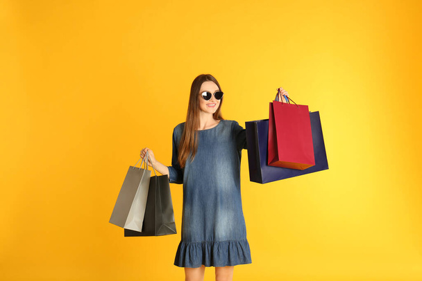 Beautiful young woman with paper shopping bags on yellow background - Fotó, kép