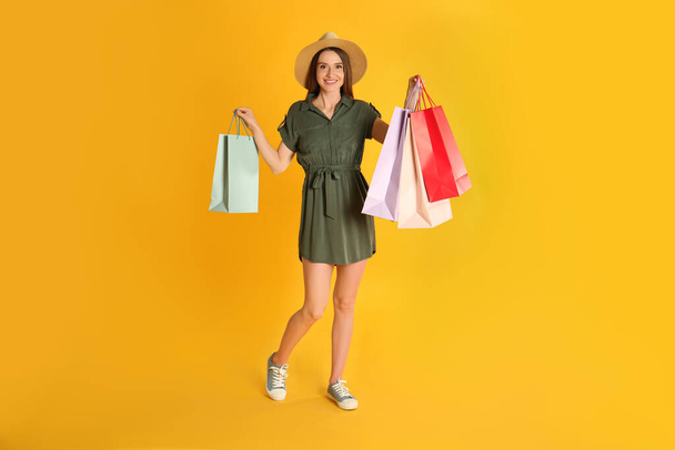 Beautiful young woman with paper shopping bags on yellow background - Foto, Bild