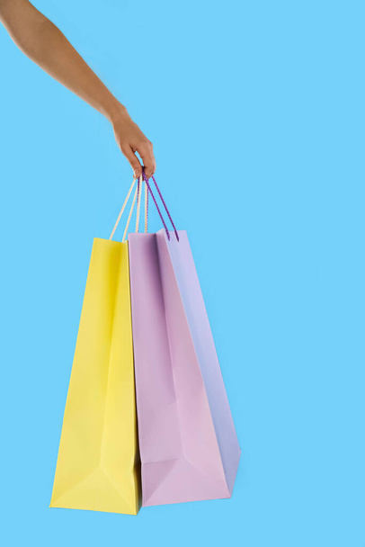 Woman with paper shopping bags on light blue background, closeup - Foto, afbeelding