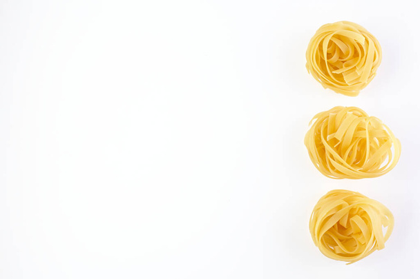 Italiaans gerold Rauwe noedels. Pasta geïsoleerd op witte achtergrond. Eieren van zelfgemaakte droge lint noedels, langgerolde macaroni of ongekookte spaghetti geïsoleerd. - Foto, afbeelding