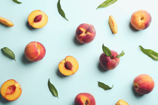 Fresh ripe peaches and green leaves on light blue background, flat lay - 写真・画像