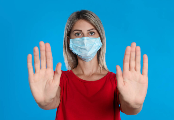 Woman in protective mask showing stop gesture on light blue background. Prevent spreading of coronavirus - Foto, Bild