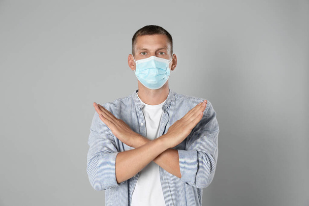 Man in protective mask showing stop gesture on grey background. Prevent spreading of coronavirus - Фото, зображення