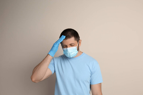 Gestresste man met beschermend masker op beige achtergrond. Geestelijke gezondheidsproblemen tijdens de COVID-19 pandemie - Foto, afbeelding
