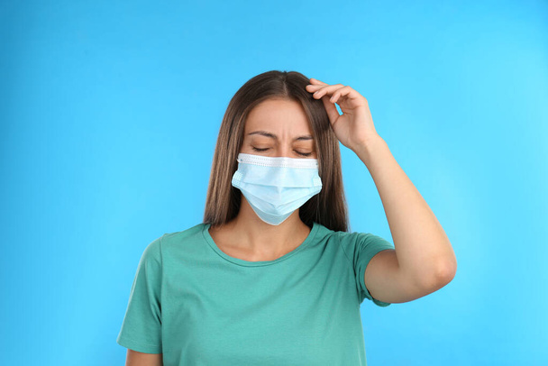 Gestresste vrouw met beschermend masker op lichtblauwe achtergrond. Geestelijke gezondheidsproblemen tijdens de COVID-19 pandemie - Foto, afbeelding