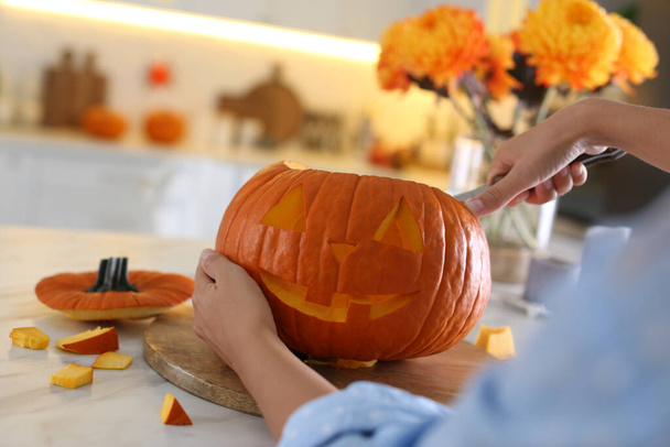 Woman making pumpkin jack o'lantern at table in kitchen, closeup. Halloween celebration - Photo, image
