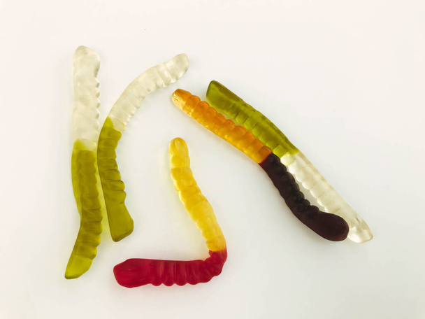 Gummiwürmer liegen auf einem weiß-matten Hintergrund. helle, köstliche gallertartige Würmer in verschiedenen Farben. leckeres und süßes Dessert. leckere Süßigkeiten - Foto, Bild