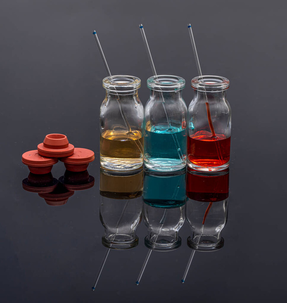 Lasiset injektiopullot, joissa on värillistä lääkeainetta ja kapillaareja. Punainen, keltainen ja sininen liuos lasisessa injektiopullossa kemian laboratoriossa. - Valokuva, kuva