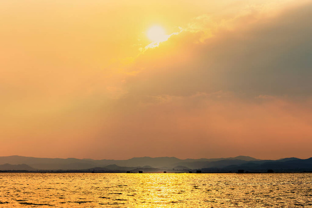 Hermoso paisaje natural el sol brilla dorado brillante en la nube refleja la luz amarilla en el cielo y el lago tropical de superficie de agua en el fondo de la montaña de verano en la presa Krasiao, Suphan Buri, Tailandia - Foto, imagen