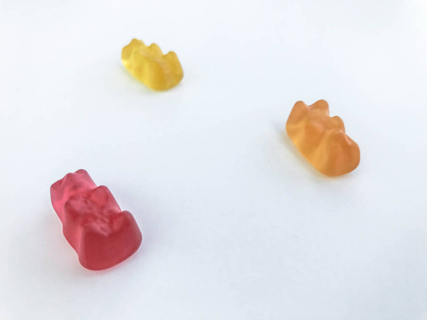 Gummibärchen auf weißem matten Hintergrund. Auf dem Tisch liegen rote, gelbe und orangefarbene Bären. leckere Süßigkeiten, Leckereien von Menschen. Bonbons aus eigener Produktion. Süßigkeiten zum Dekorieren von Kuchen und Gebäck - Foto, Bild
