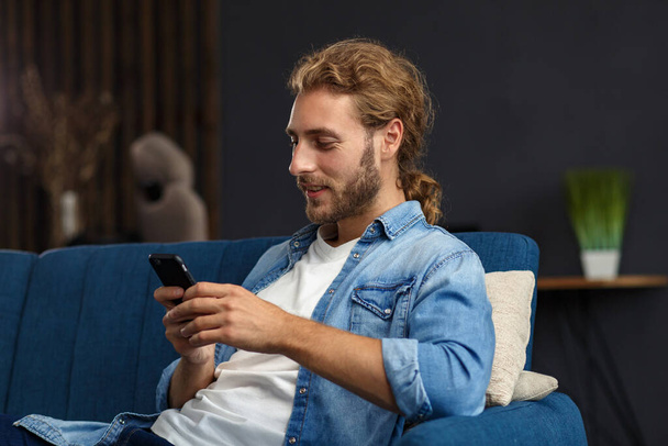 Curvy guy using smartphone and smiling. Happy man using mobile phone apps, texting message, browsing internet, looking at smartphone, sitting at home. Young people working with mobile devices - Photo, image