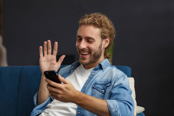 Curvy guy using smartphone and smiling. Happy man using mobile phone apps, texting message, browsing internet, looking at smartphone, sitting at home. Young people working with mobile devices - Photo, Image