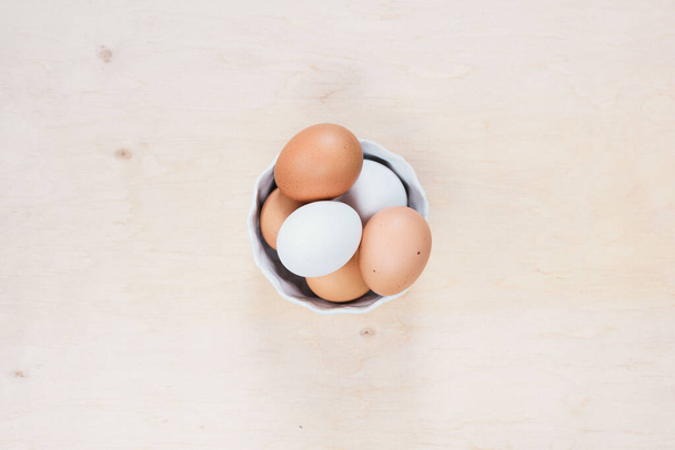 卵は木製の背景に置かれる。食材。木製の背景にボウルに生の鶏の卵のクローズアップビュー. - 写真・画像
