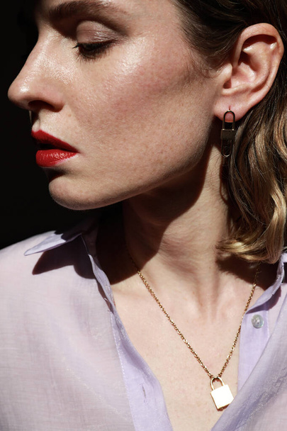 Side portrait of attractive young woman with red lips wearing golden jewellery. Vertical close-up of beautiful woman. - Φωτογραφία, εικόνα