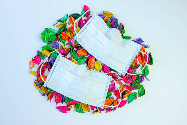 Medizinische Maske, Medizinische Schutzmaske auf weißem Hintergrund mit getrockneten farbigen Blumen. - Foto, Bild