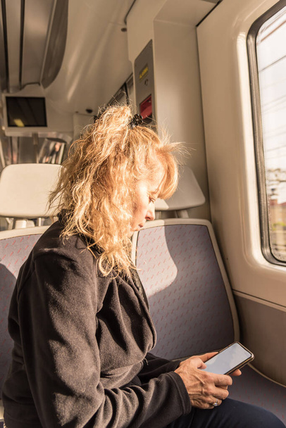 Adult woman traveling alone on the train looking at a mobile. Concept of new naturally - Photo, Image