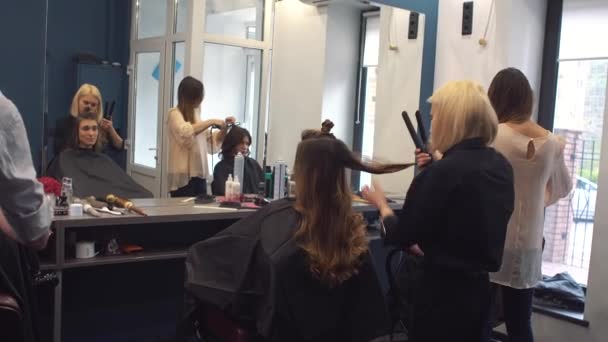 piękno, koncepcja fryzury, szczęśliwa młoda kobieta i fryzjer z żelaza do włosów fryzurę w salonie fryzjerskim. Kobieta o włosy stylizowane fryzjer. Wygładza włosy curling. Stylista za pomocą narzędzia do modelowania - Materiał filmowy, wideo