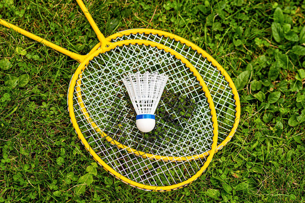 white shuttlecock close-up on yellow badminton rackets in the green grass, top down view - Fotó, kép