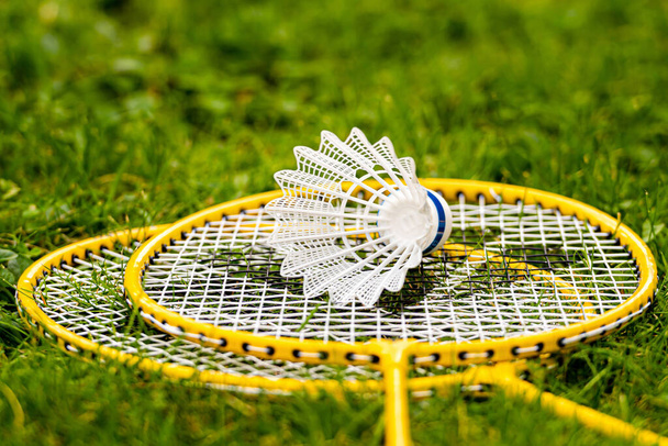 white shuttlecock on yellow badminton rackets in the green meadow - Фото, изображение
