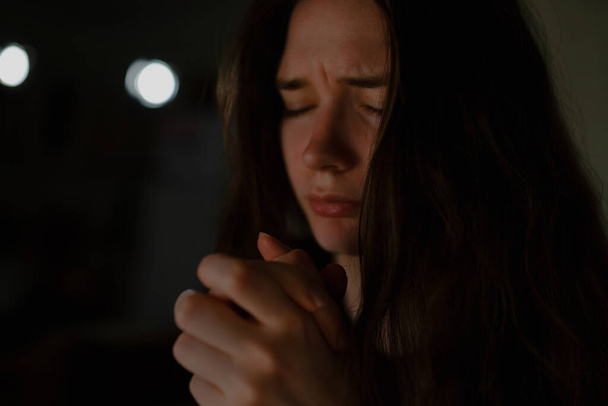 Nuori nainen rukoilee Jumalaa asunnossa yöllä, lähikuva. - Valokuva, kuva