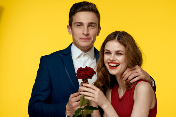 amantes hombre y mujer con una rosa roja en sus manos abrazándose en un fondo amarillo romance relación amor familia - Foto, Imagen