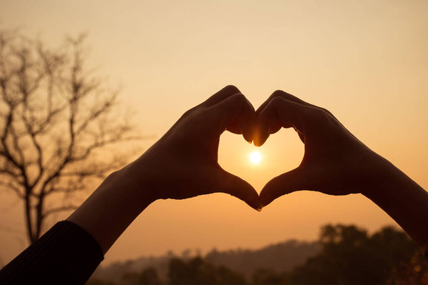 Руки делают в форме сердца любовь с силуэтом на фоне заката солнца - Фото, изображение