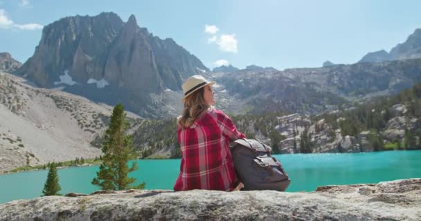 Woman enjoying cinematic nature view. Back view traveler sitting at blue lake 4K - Footage, Video