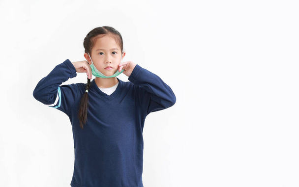 Asian little kid girl wearing medical face mask slung on her chin isolated on white background. Amid covid-19 pandemic concept - Fotó, kép
