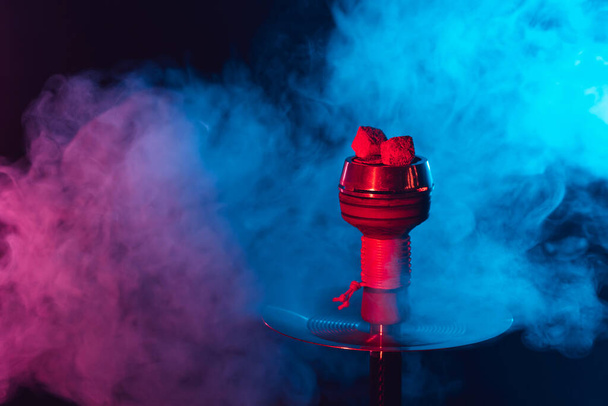 червоне гаряче шашликове вугілля в металевій мисці для кальяну на фоні різнокольорового диму
 - Фото, зображення