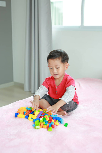 Portrait of asian little baby boy playing colorful plastic blocks and lying on bed - Fotó, kép